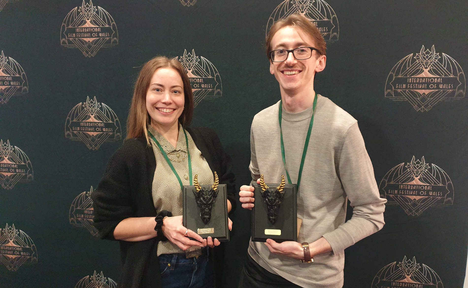 Female and male filmmakers smiling with awards statuettes
